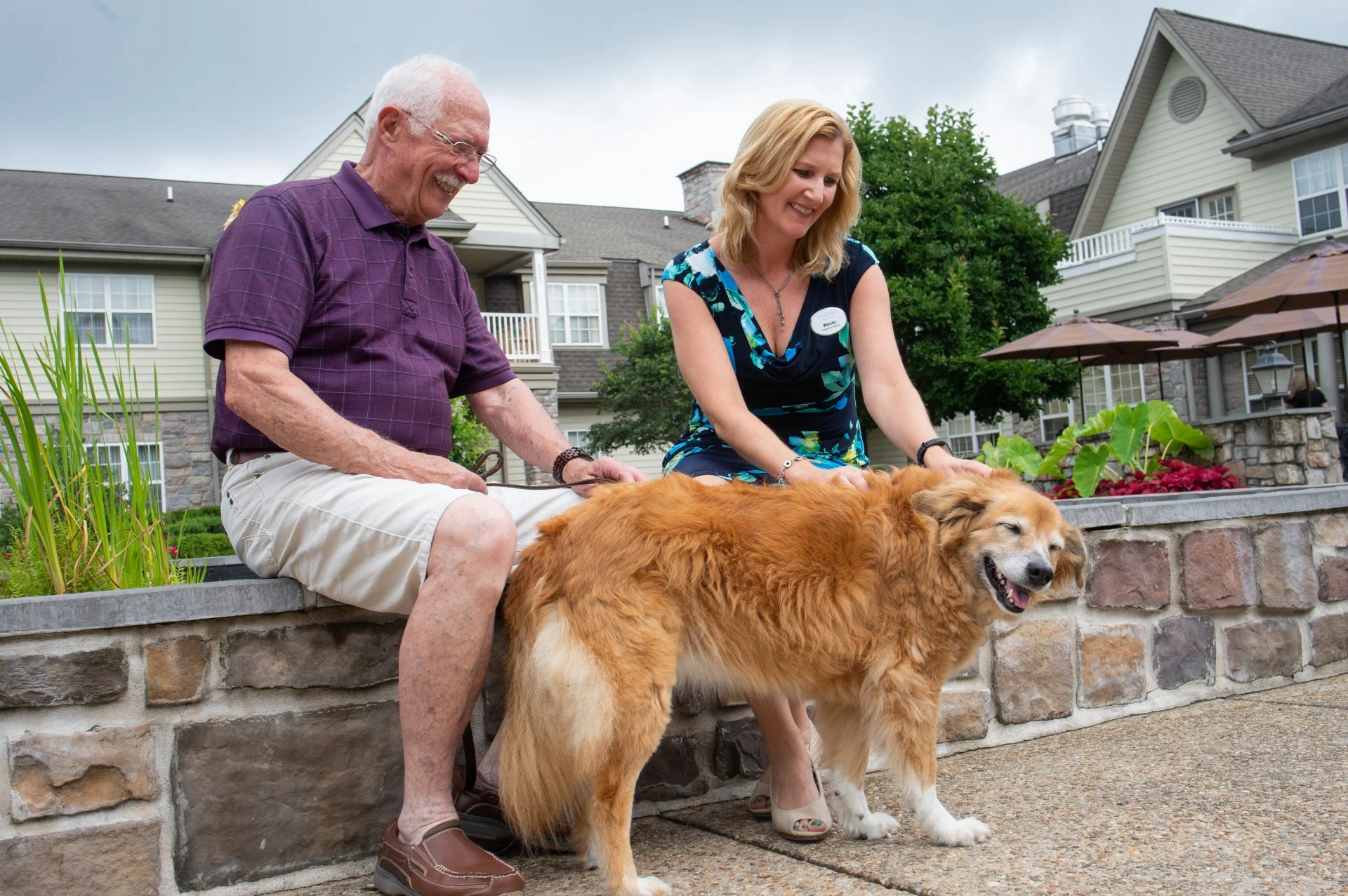 A resident and the executive director of The Manor at York Town pet a golden retriever outside.