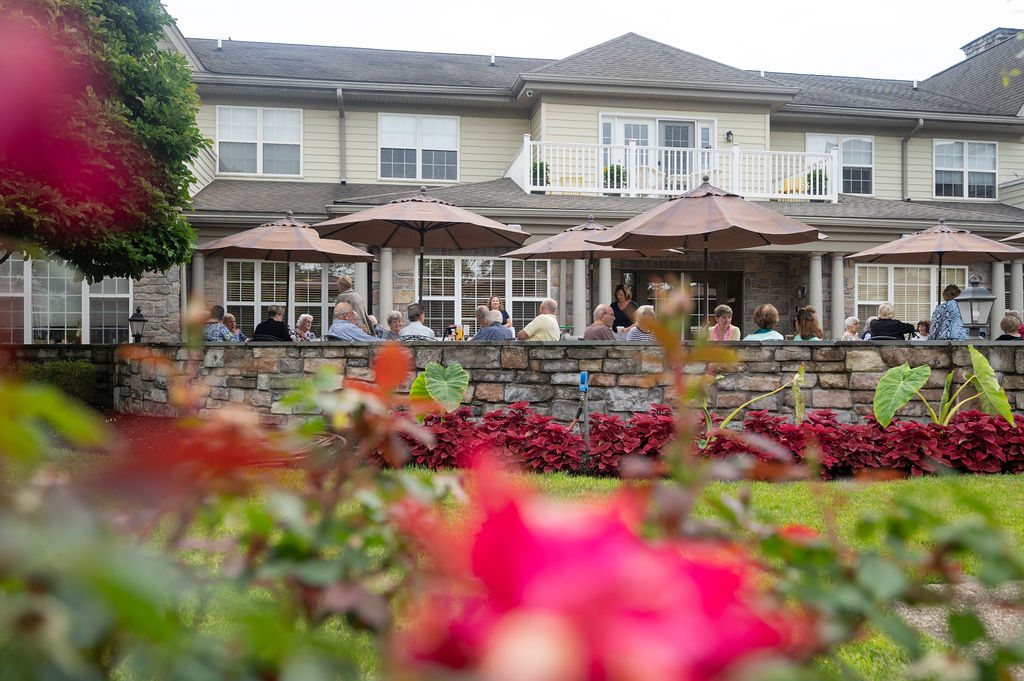 Pink flowers and residents sitting outside during The Manor at York Town's weekly happy hours