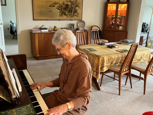 An older woman plays the piano in an apartment.